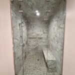Glass-enclosed marble shower with bench, mosaic floor