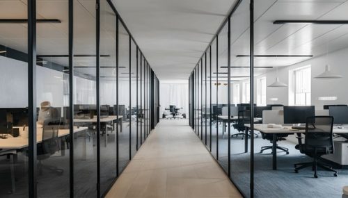 Modern glass-walled office corridor with workstations
